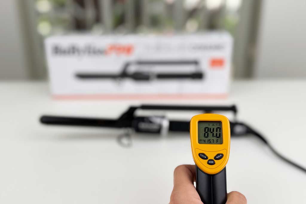 Infrared thermometer reading 84°F on the handle of the BaBylissPRO Porcelain Marcel Curling Iron.