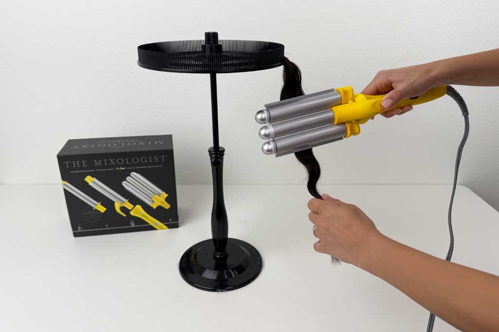 Hands using the Drybar Mixologist triple waver on a human-hair wig, forming S-waves during testing.