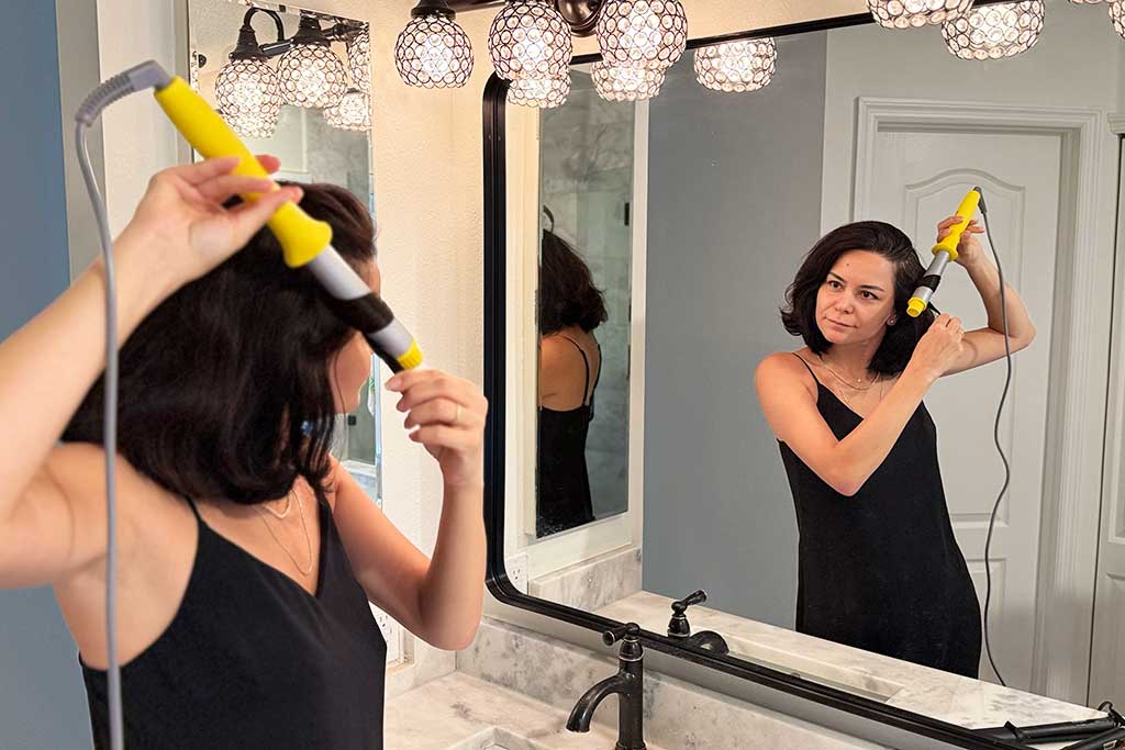 Woman using the Drybar Wrap Party curling wand on mid-length hair, demonstrating comfort and relaxed wave results.