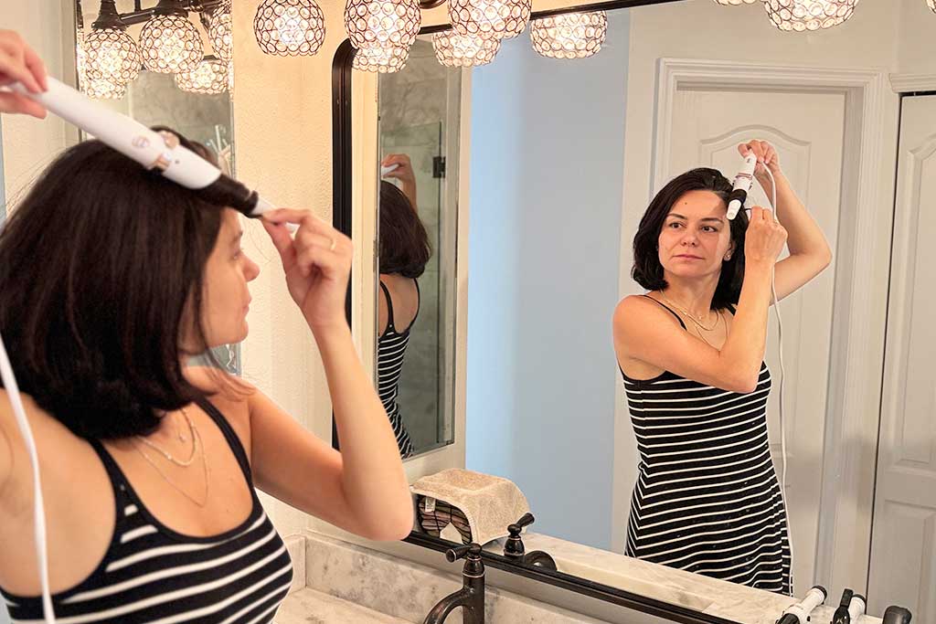 Person styling their own hair with the T3 SinglePass Wave curling wand, showing comfortable grip and wave results.