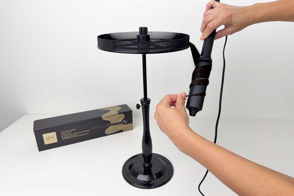 Woman styling mid-length hair with the GHD Classic Wave Wand, wrapping sections around the oval barrel to form polished waves.
