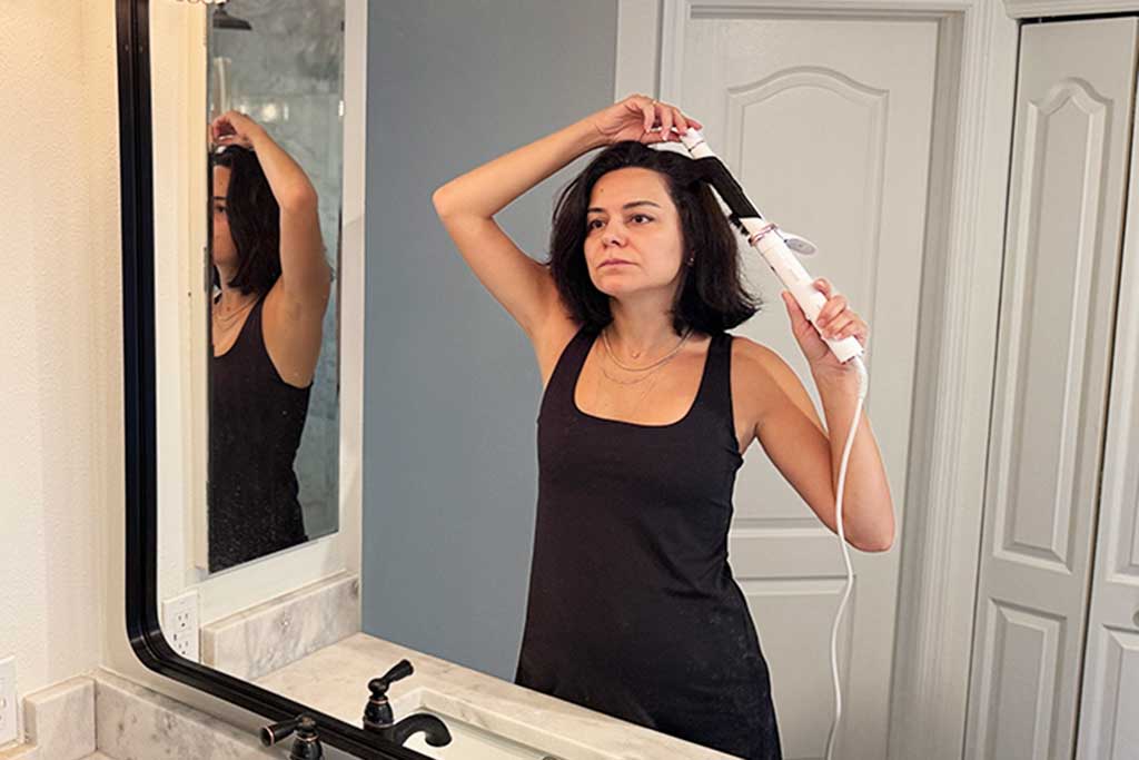 Person styling their own long hair with the T3 CurlWrap curling iron, showing easy automatic rotation.