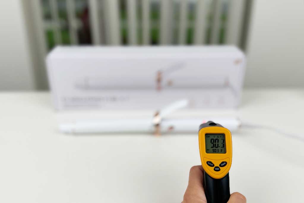 Infrared thermometer reading 90°F pointed at the handle of the T3 SinglePass Curl X curling iron.