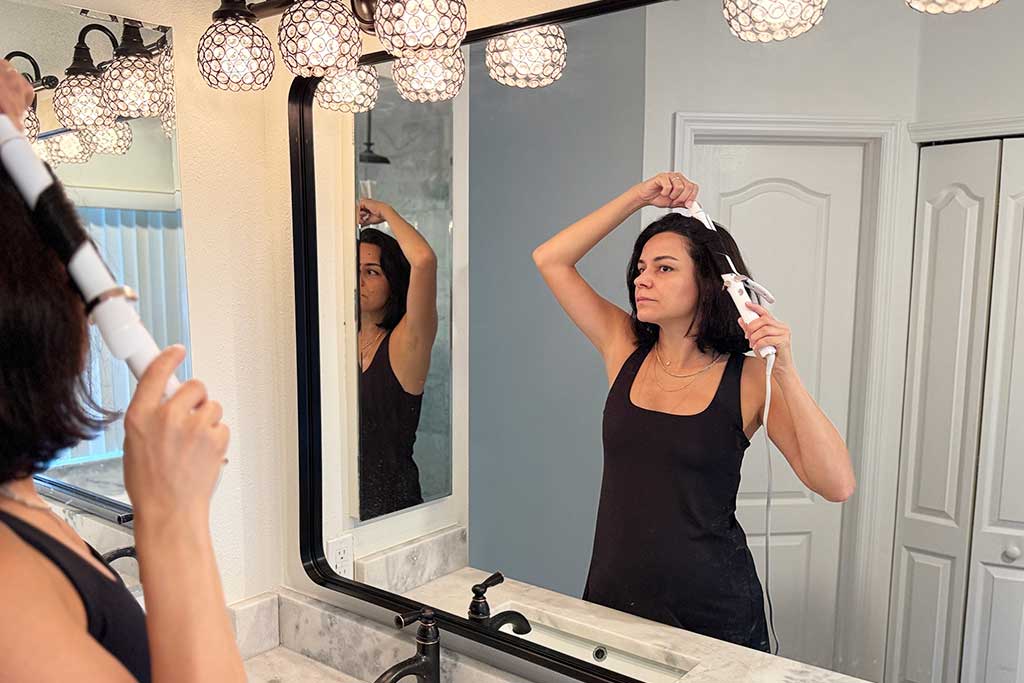 Person styling shoulder-length hair with the T3 SinglePass Curl X curling iron, showing smooth curls forming around the extra-long barrel.