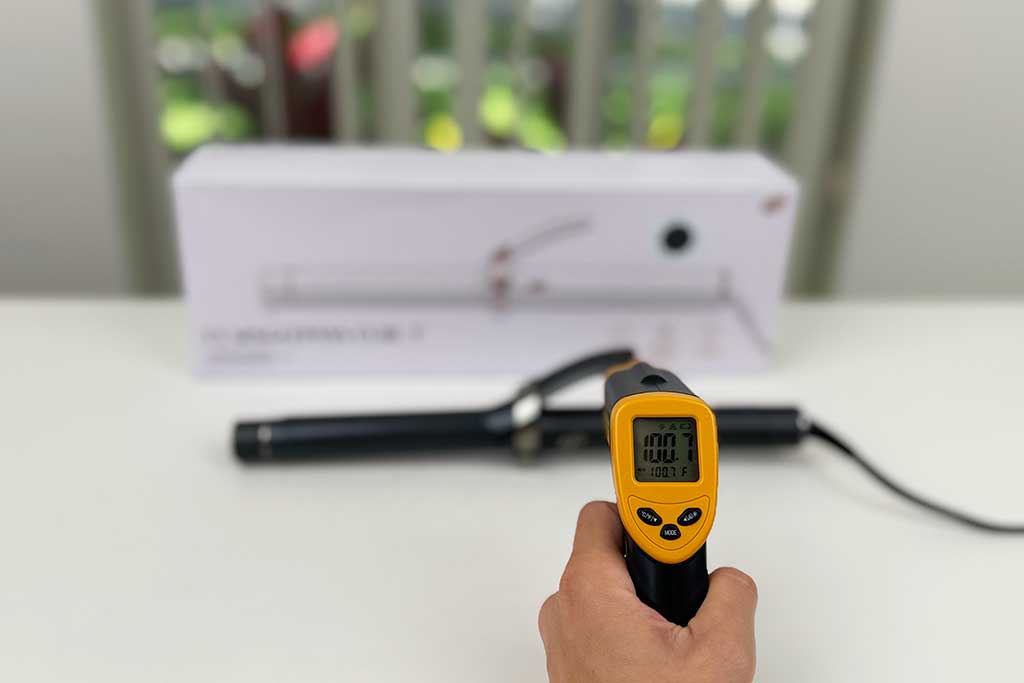 Infrared thermometer reading 100°F pointed at the finger grip of the T3 SinglePass Curl curling iron.