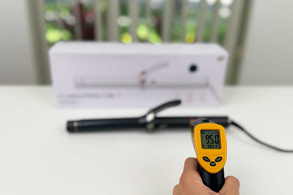 Infrared thermometer reading 95°F pointed at the handle of the T3 SinglePass Curl curling iron.